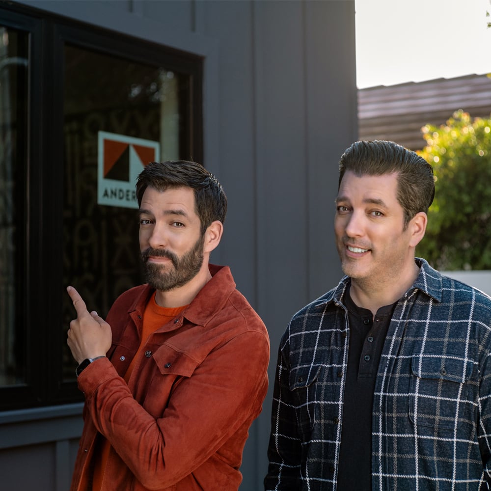 Drew and Jonathan Scott standing in front of new home with Andersen Windows stickers on the windows